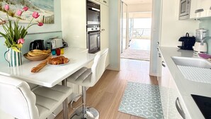 A modern kitchen with white cabinetry, a dining area with a white table and bar stools, and a view of the balcony. - Face mer à La Baule : Le Neptune (La Baule-Escoublac)