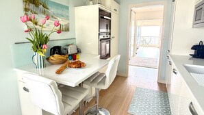 A modern kitchen with white cabinets, a dining table with chairs, a vase of flowers, and a painting on the wall. - Face mer à La Baule : Le Neptune (La Baule-Escoublac)