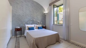Une chambre avec un mur incurvé, un lit doté d’une tête de lit blanche, deux tables de chevet et une fenêtre avec des rideaux.