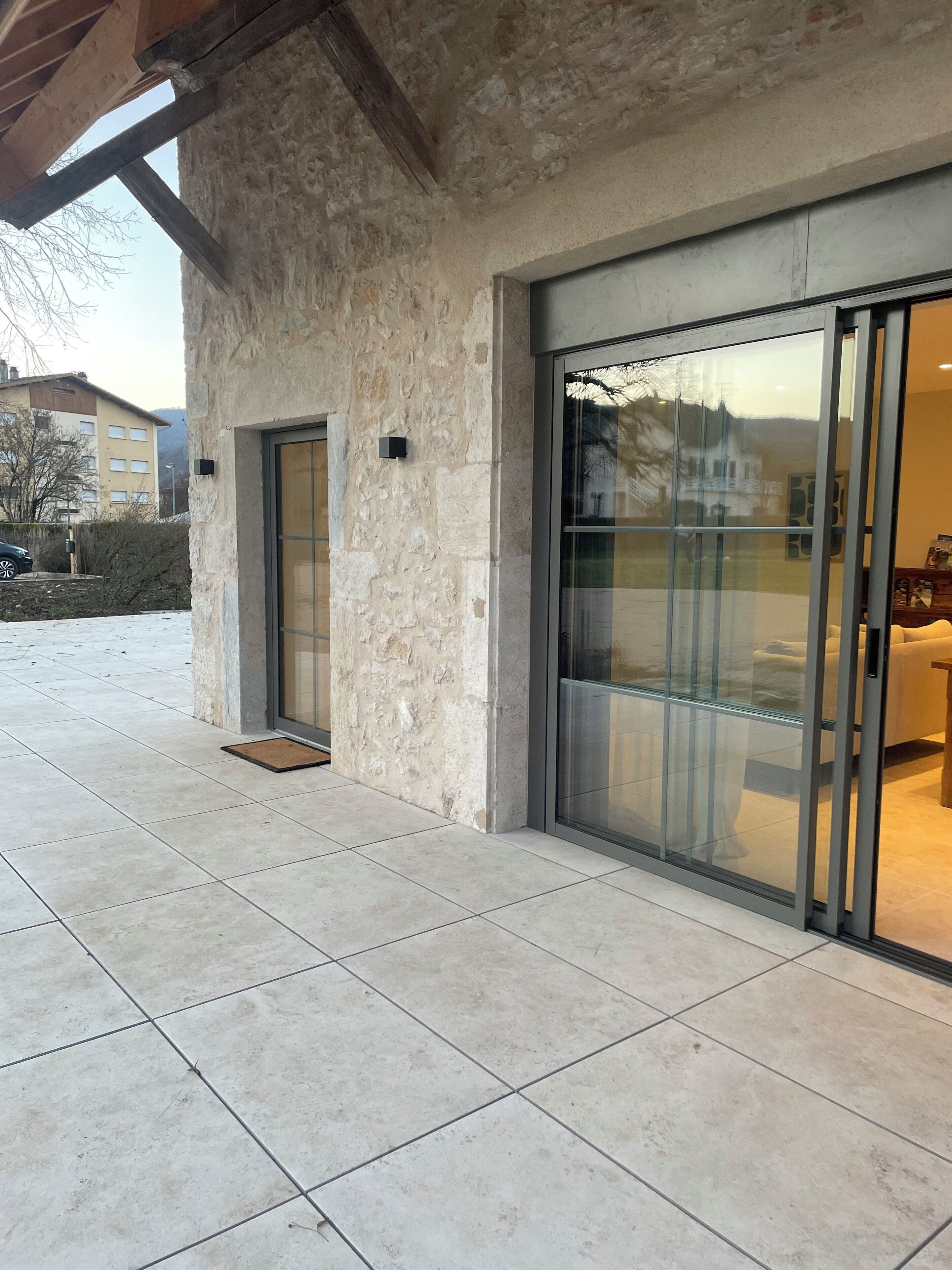 Un edificio moderno con paredes exteriores de piedra, un amplio cristalero corredero y un patio con baldosas.