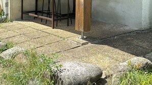 A covered outdoor seating area with a wooden table and chairs, a sign reading "L'ORRY", and a stone wall.