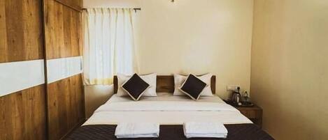 A bedroom with a wooden wardrobe, a bed with white bedding, a ceiling fan, and an air conditioning unit.