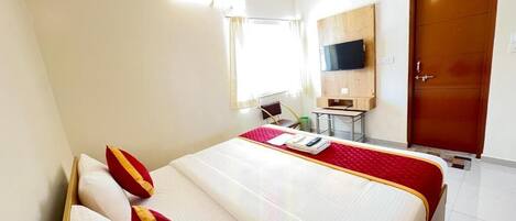 Una habitación de hotel con cama, televisor montado en la pared, escritorio y armario.