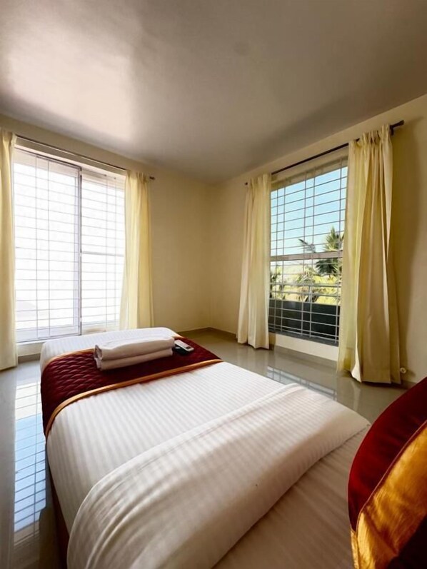 A hotel room with a large bed, two windows with curtains, and a view of palm trees outside.