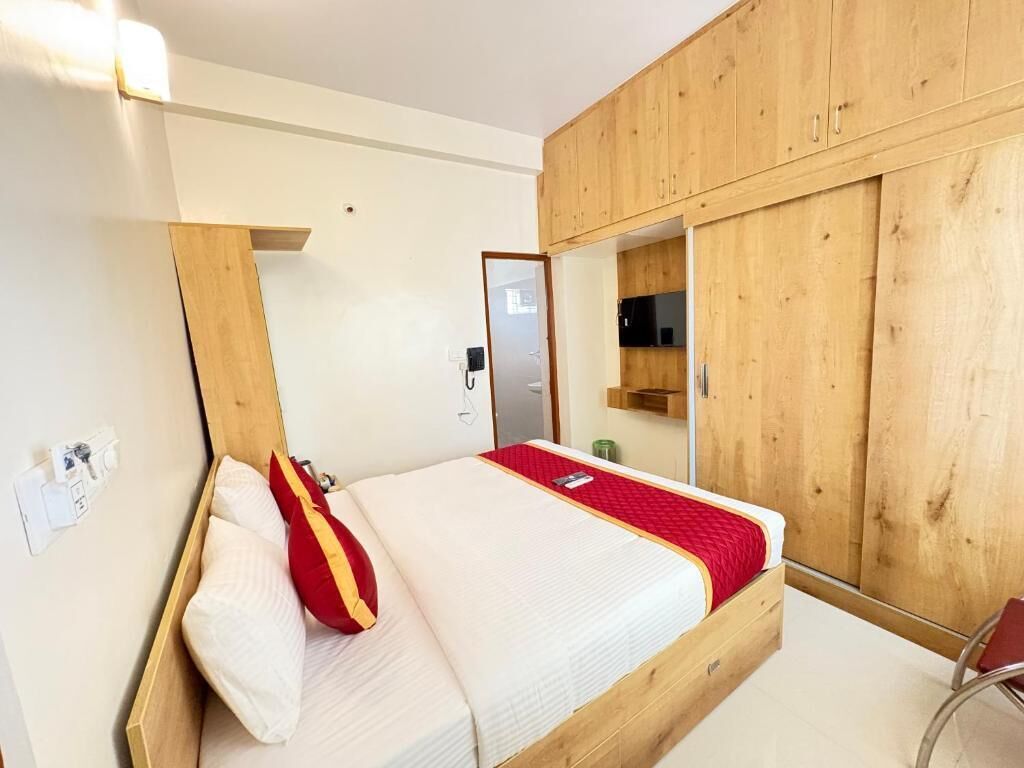 A bedroom with a wooden bed frame, a red and white pillow, a bedside table, and a wardrobe with a mirror.