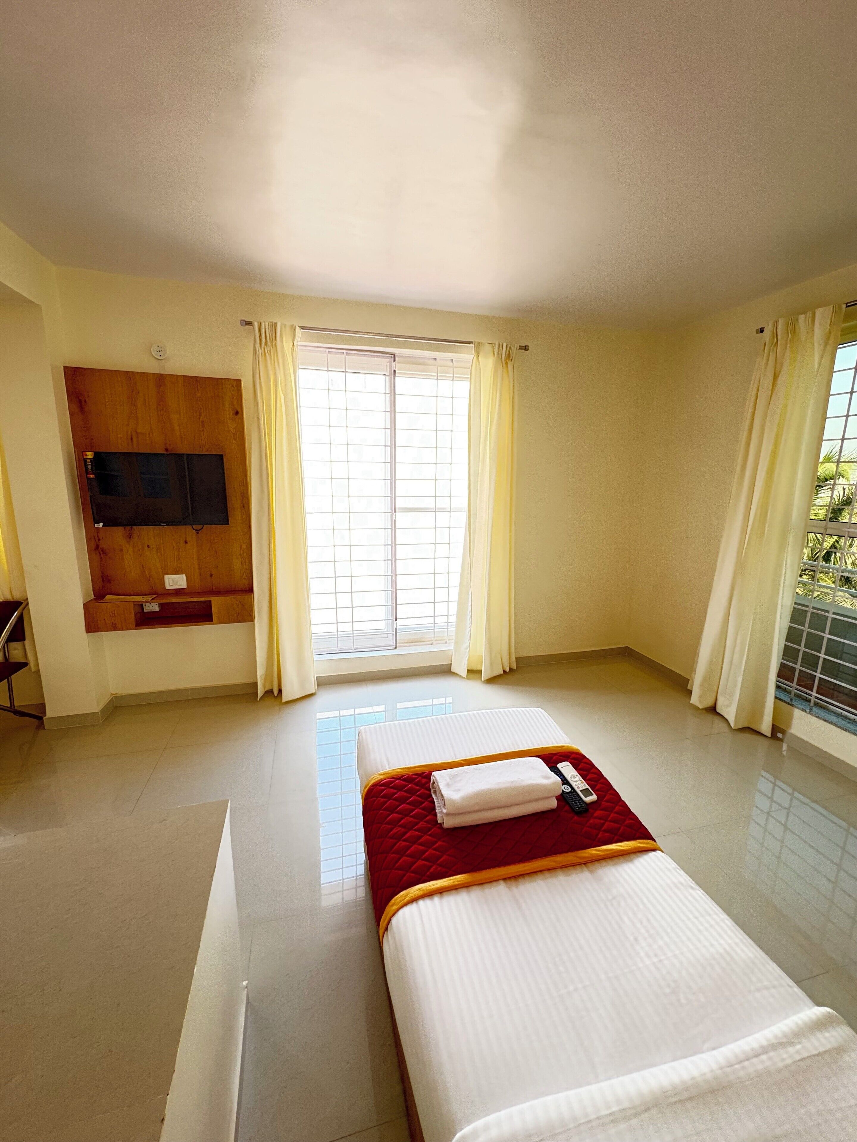 A hotel room with a bed, a TV mounted on the wall, and a window with curtains.
