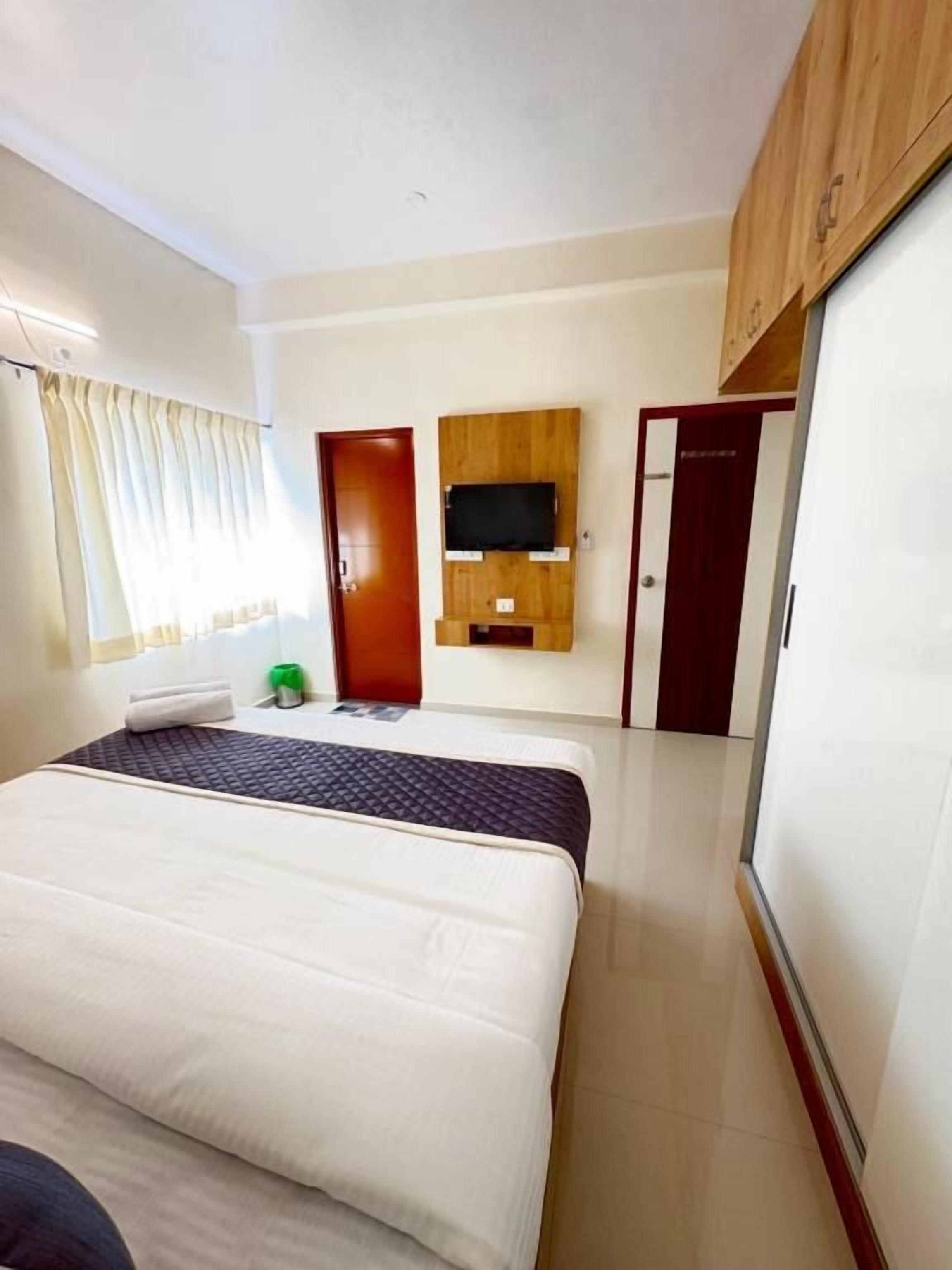 A hotel room with a bed, a TV mounted on the wall, a wardrobe, and a door.