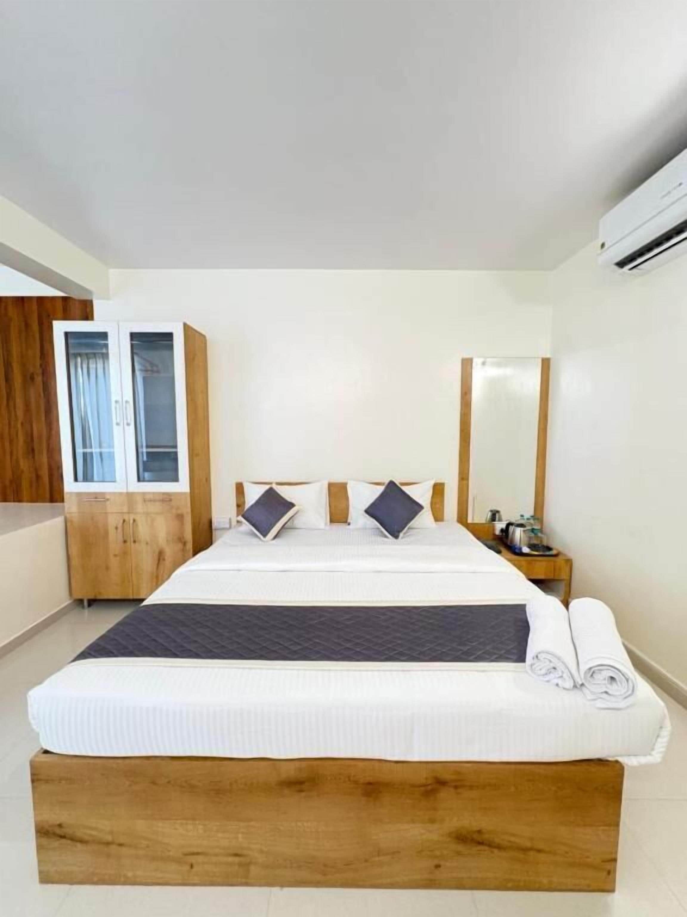 A hotel room with a large bed, wooden headboard, a wardrobe, a bedside table, and a mirror.