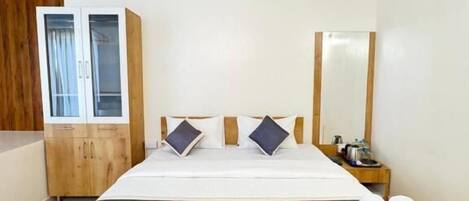 A hotel room with a large bed, wooden headboard, a wardrobe, a bedside table, and a mirror.