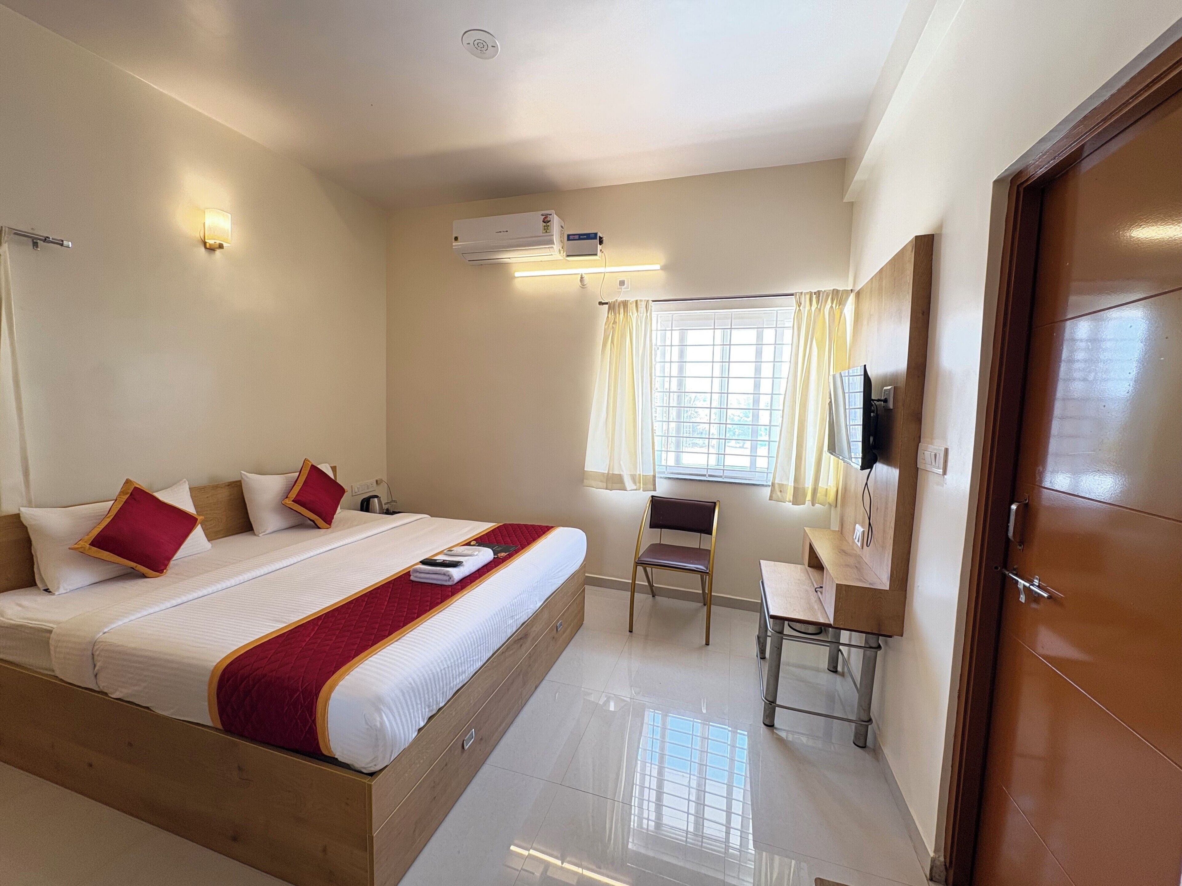 A hotel room with a large bed, a desk, a chair, a television, and a window with curtains.
