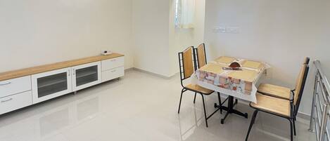 A spacious room with a dining table, chairs, a ceiling fan, and a bench along the wall.