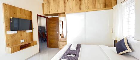 A modern hotel room with a large bed, a TV mounted on a wooden panel, and a wooden wardrobe.