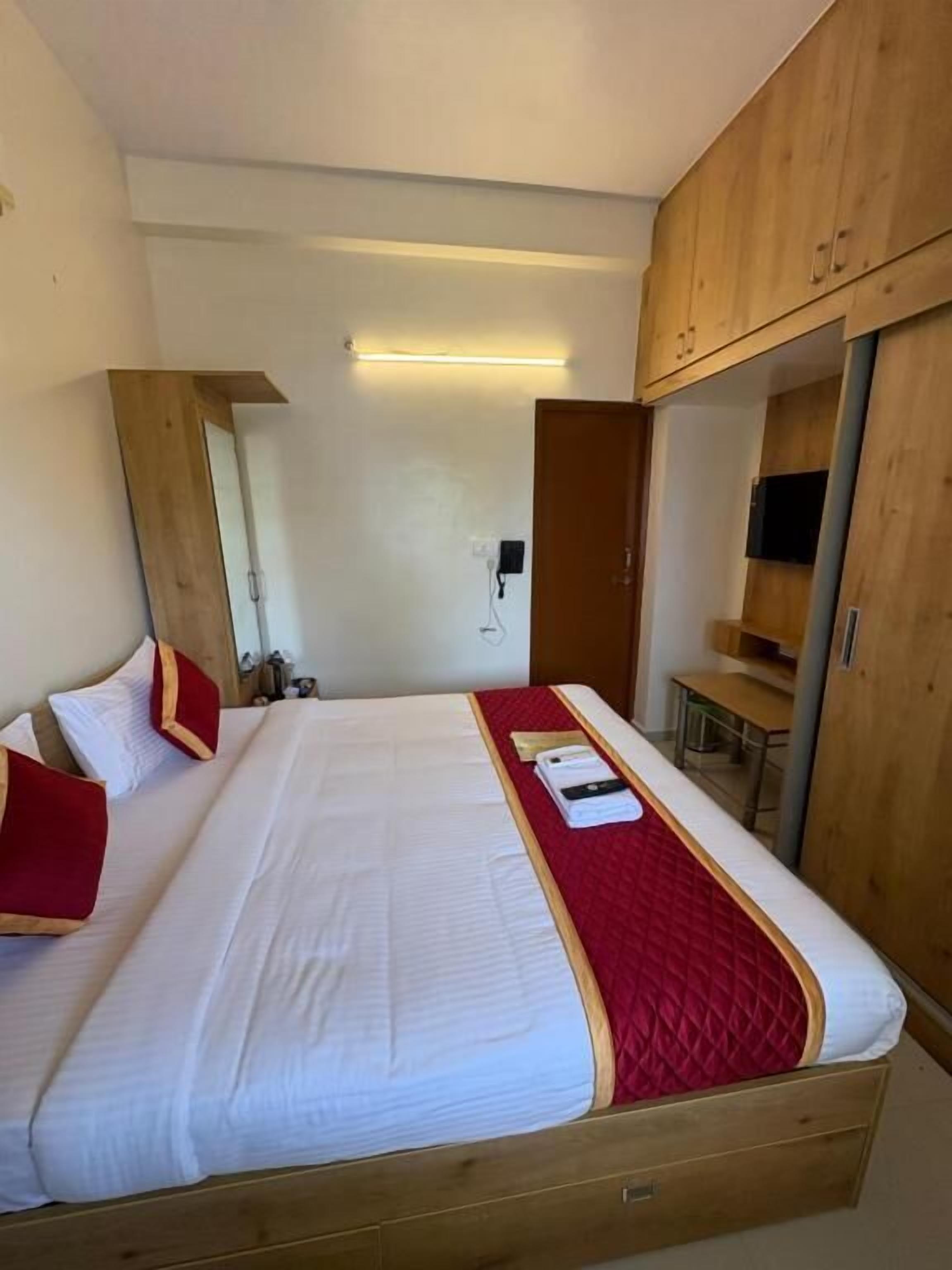 Ein ordentlich bezogenes Bett mit roter Decke, einem Holzkopfende und einem Nachttisch mit Lampe.