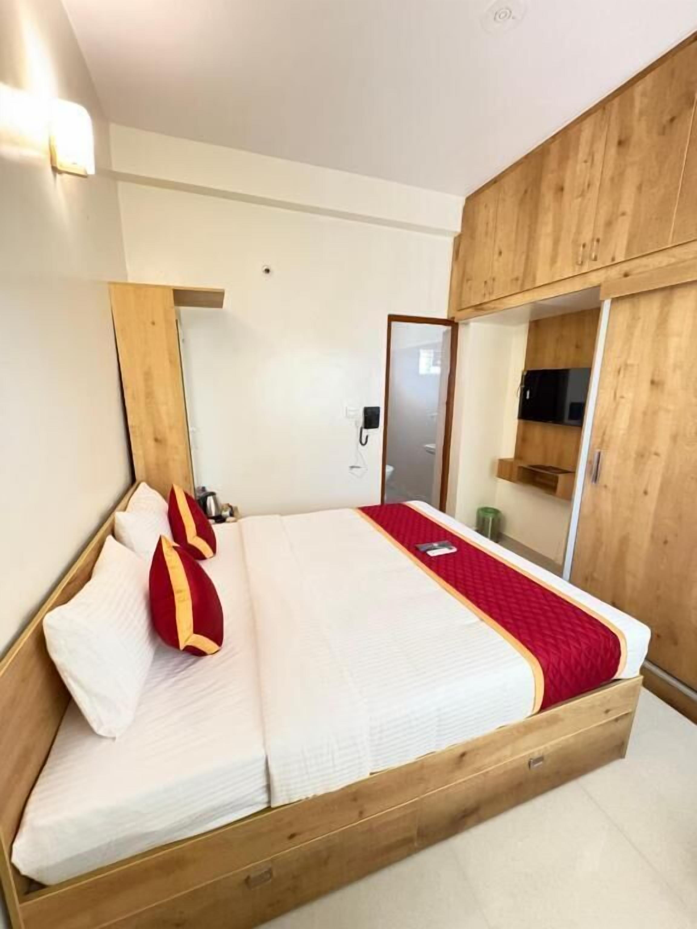 Een slaapkamer met een houten bedframe, een rode spreidek en een grote spiegel.
