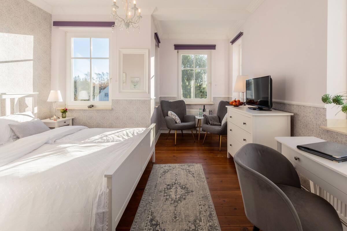 Un dormitorio con una cama, un escritorio, dos sillas, un televisor y una ventana.