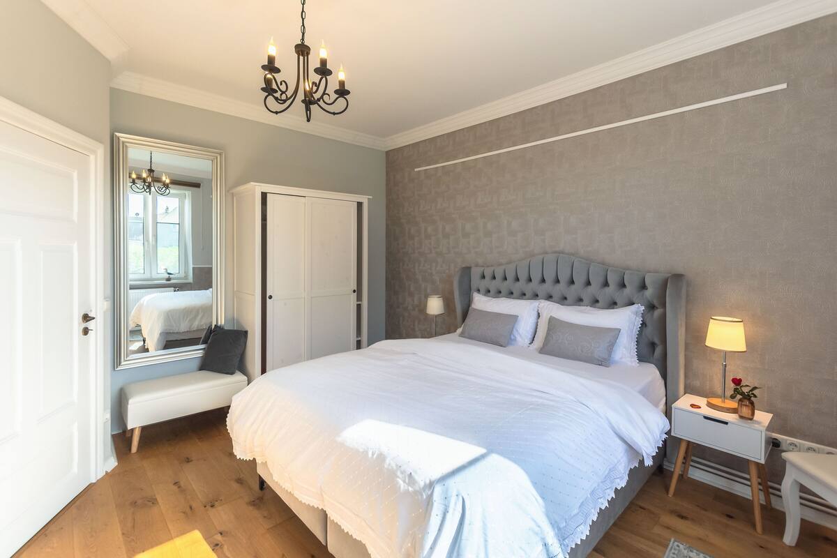 Un dormitorio con una cama grande, una mesita de noche con lámpara, un banco y un espejo.