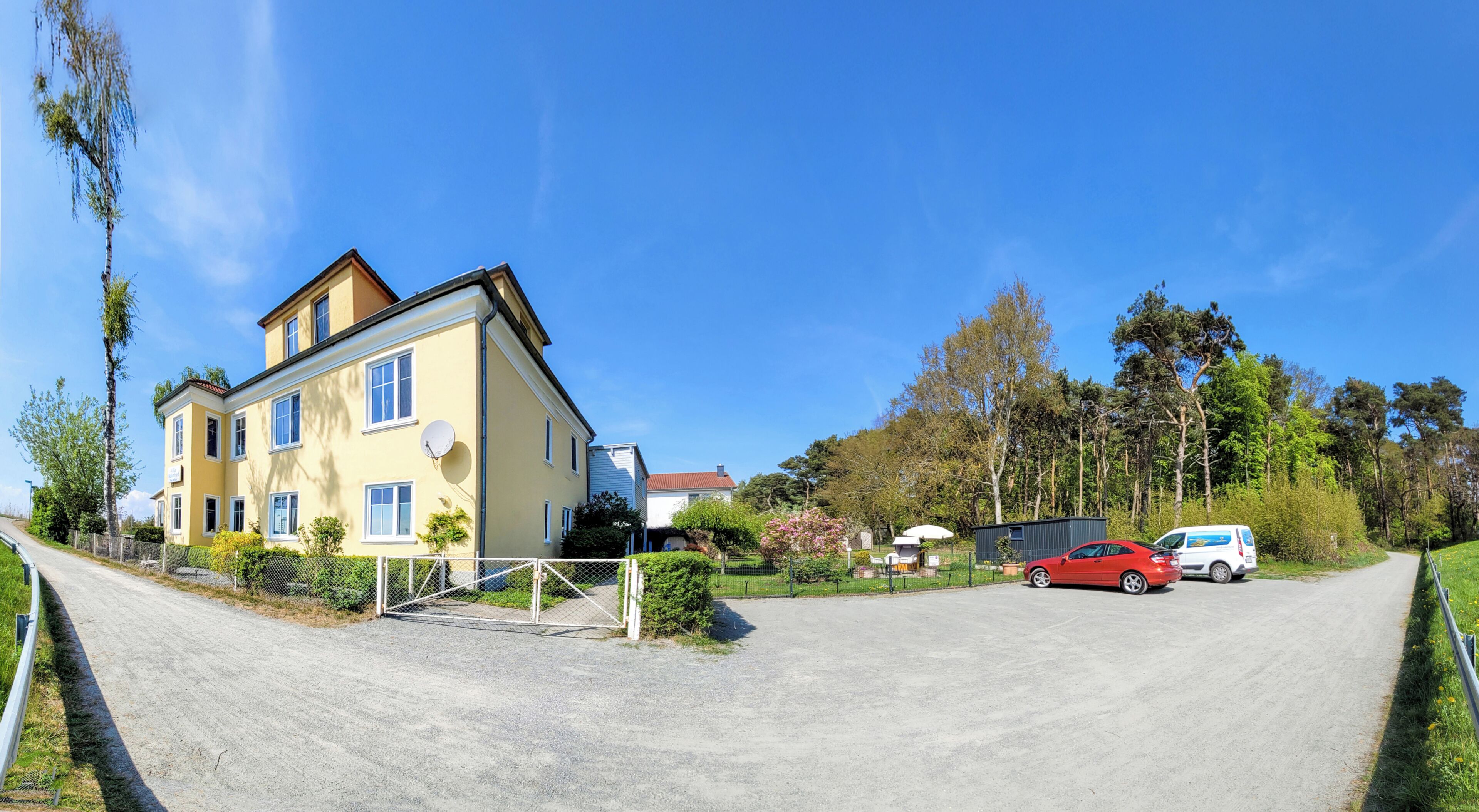 Ein zweistöckiges Gebäude mit einer gelben Fassade, ein rotes Auto davor und ein klarer, blauer Himmel.