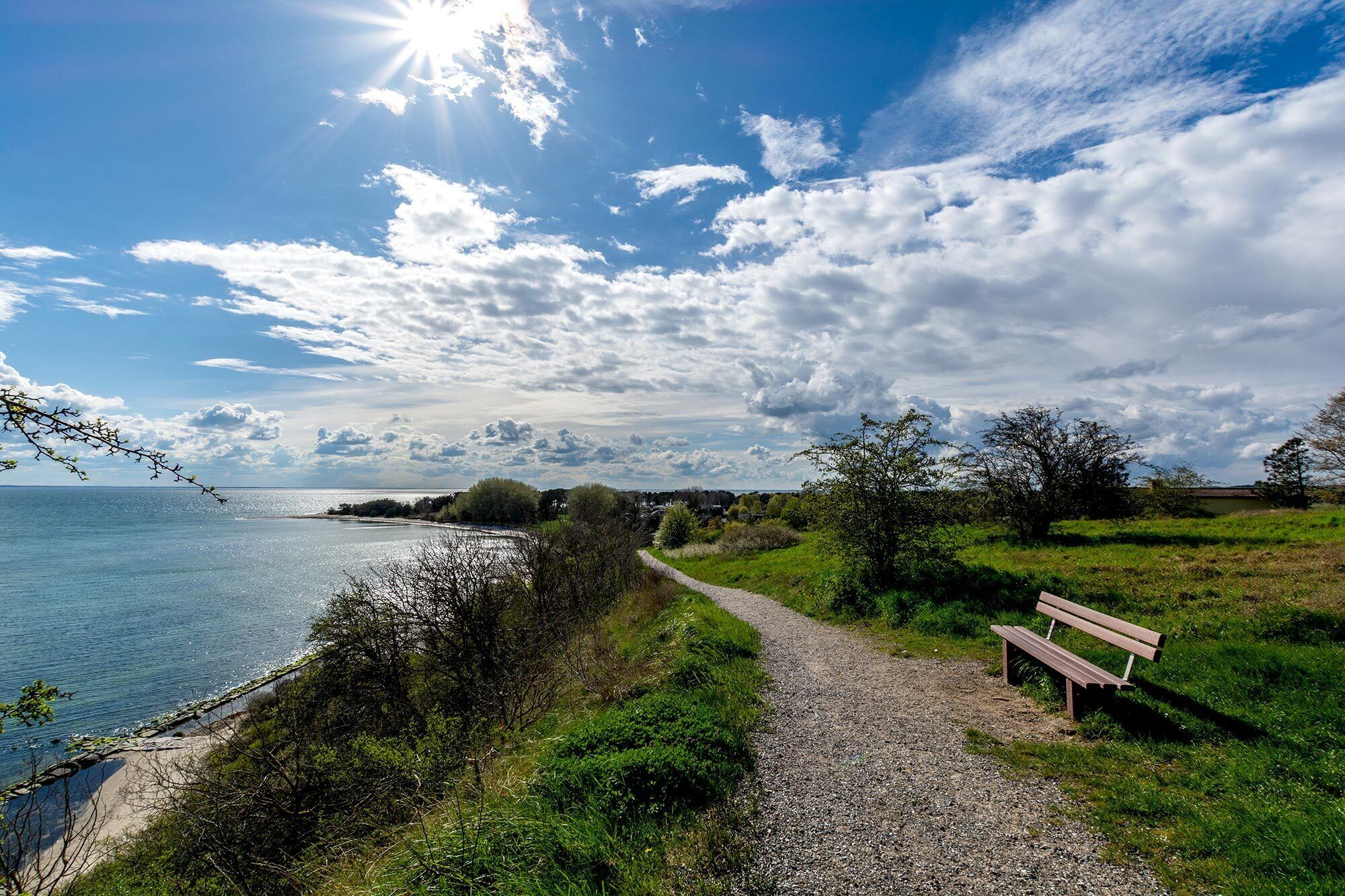 A coastal path with a bench, clear sky, and a view of the sea.