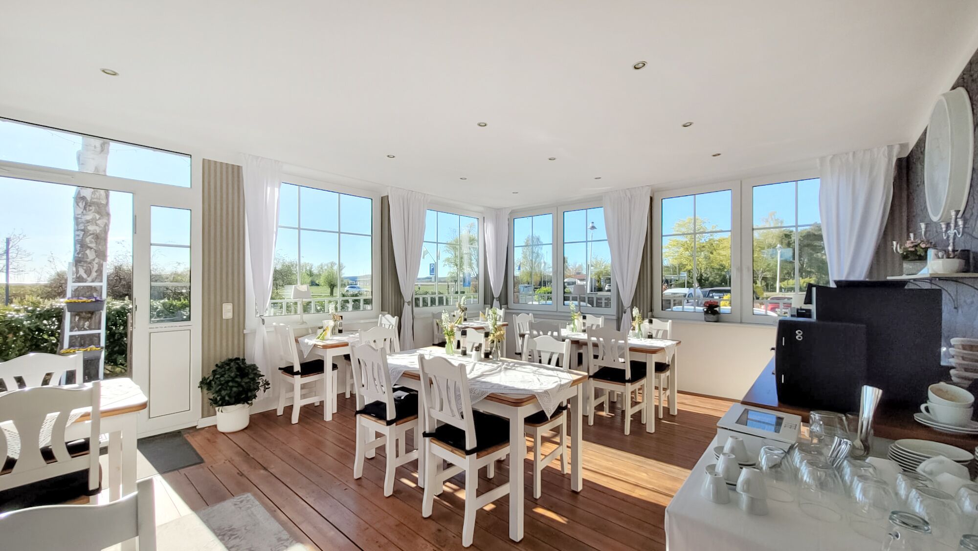 Una luminosa sala da pranzo con ampie finestre, arredi bianchi e vista sull'esterno.