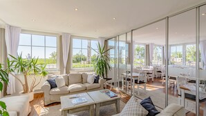 A spacious living area with a large window, a sofa, a coffee table, and a dining area with chairs. - Hotel Villa Wahnfried (Monchgut-Granitz)