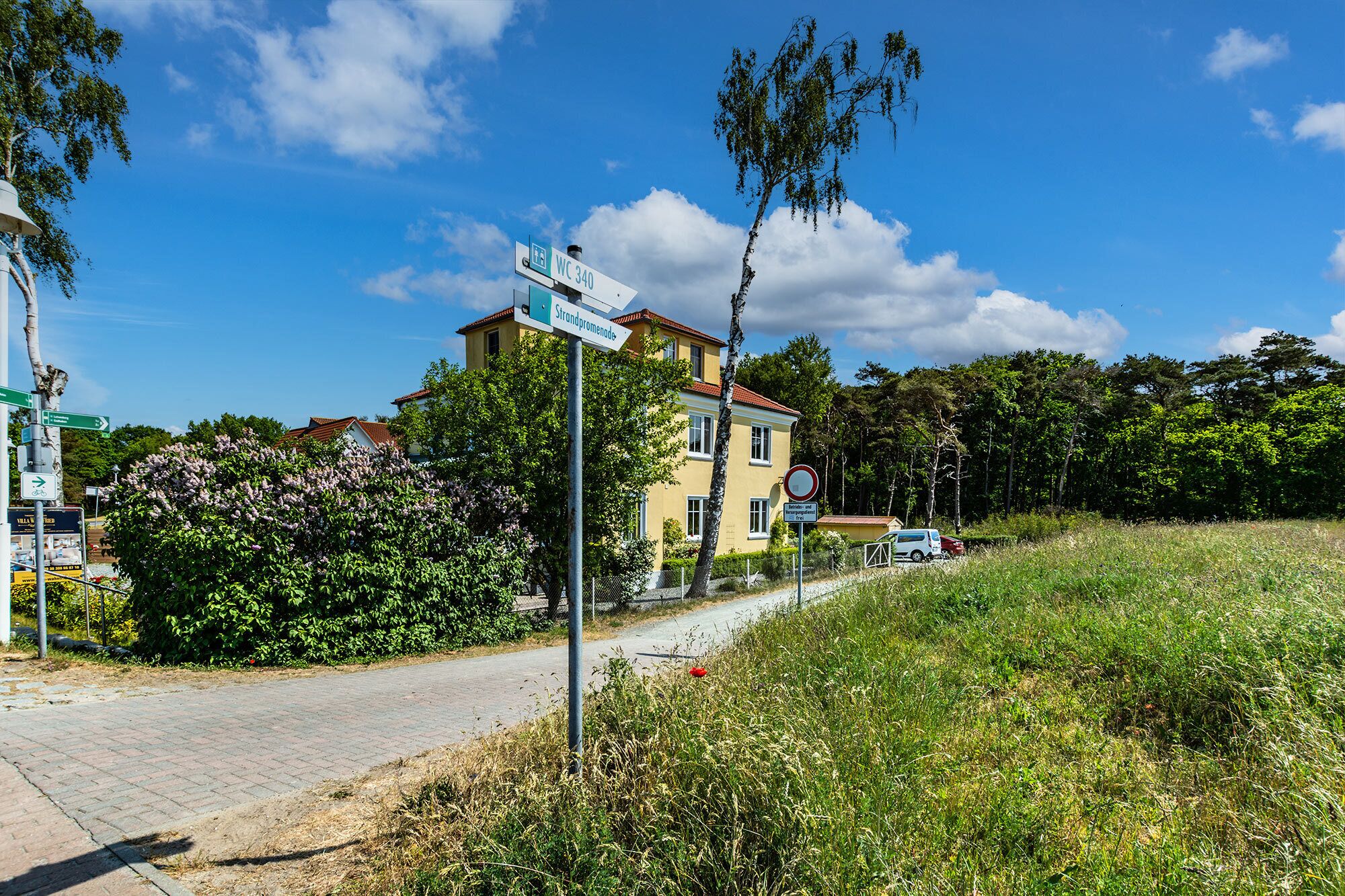 Ein Straßenschild mit der Aufschrift WC 340 und Strandpromenade, ein gelbes Gebäude und ein rotes Auto, das am Straßenrand geparkt ist.