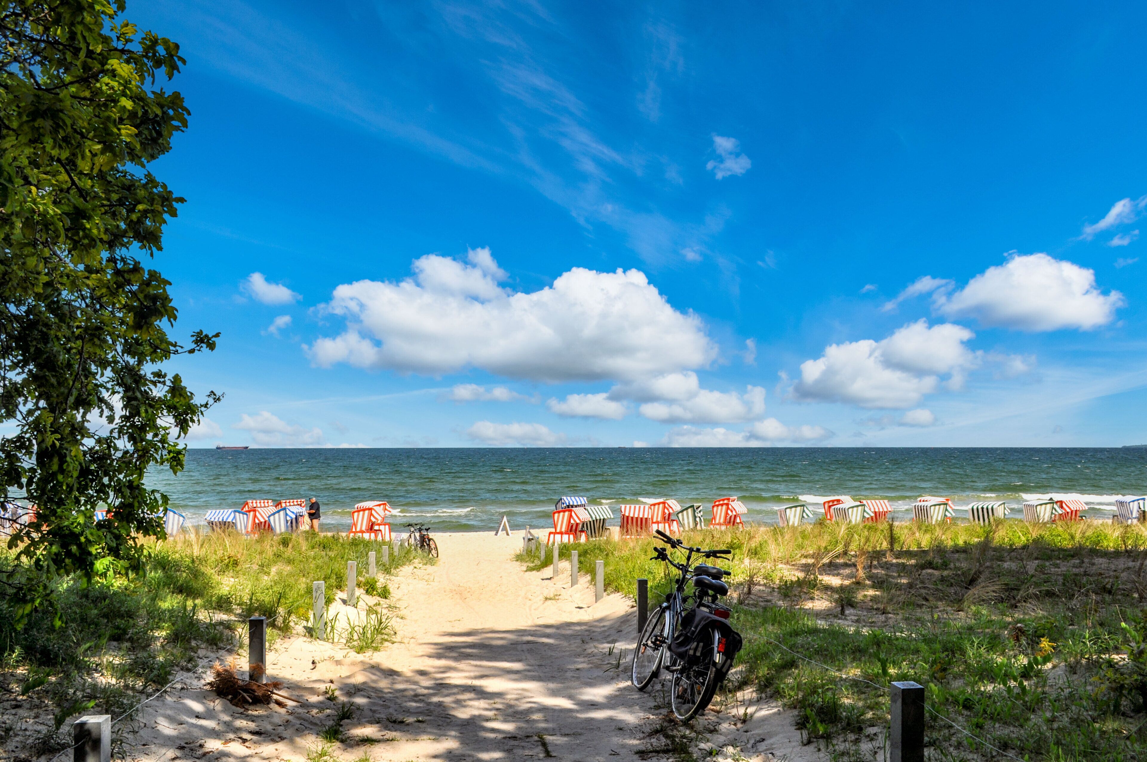 Un sendero en la playa que lleva a sillas de playa, una bicicleta y una zona arenosa con vistas al mar.