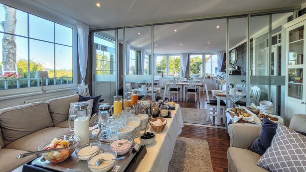 A modern dining area with a buffet setup, large windows, and a view of the outdoors. - Hotel Villa Wahnfried (Monchgut-Granitz)