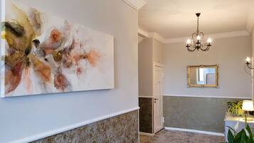 A hallway with a large abstract painting, a chandelier, a mirror, and a potted plant.