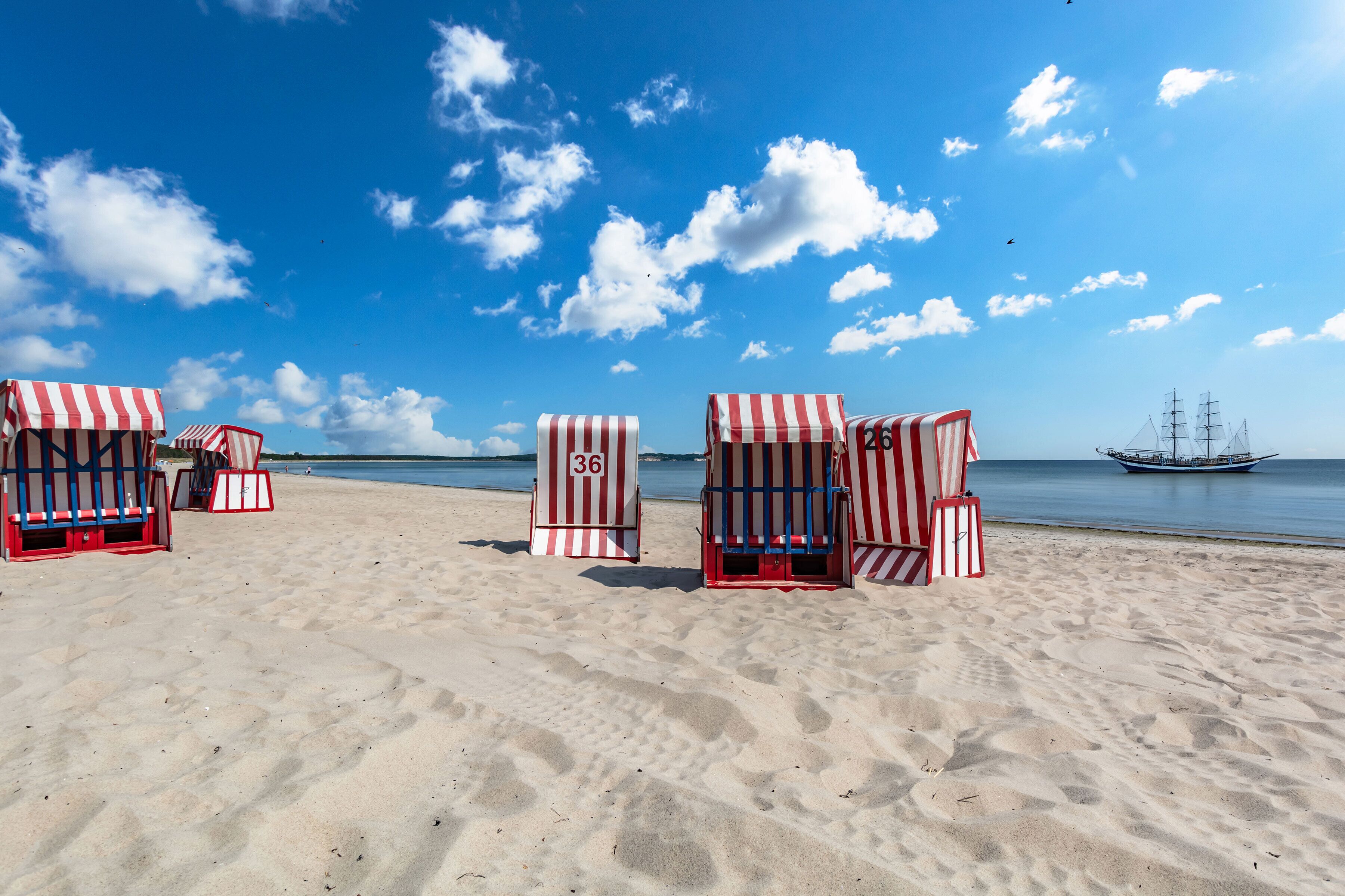 Des chaises de plage avec des auvents à rayures, une plage de sable et un navire en arrière-plan.