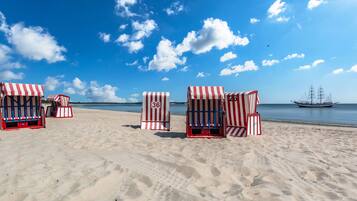 Des chaises de plage avec des auvents à rayures, une plage de sable et un navire en arrière-plan.