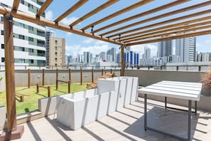 Eine Dachterrasse mit einer Holz-Pergola, einem Sitzbereich aus Beton und Blick auf die Stadtlandschaft.