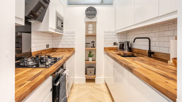A modern kitchen with white cabinets, wooden countertops, a built-in stove, and a clock on the wall. - Warm, Upgraded Top-floor Flat in Finnieston (Glasgow)
