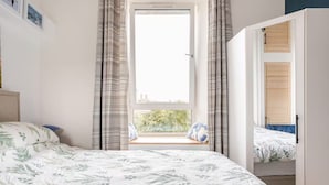 A bedroom with a large bed, a window seat, and a view of greenery outside. - Warm, Upgraded Top-floor Flat in Finnieston (Glasgow)