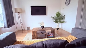 A living room with a wooden coffee table, a television, a potted plant, and a sofa. - Cosy 2 Bedroom Apartment by Airport & Town Centre (Luton)