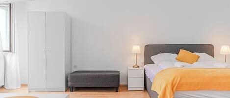 Une chambre à coucher comprenant un lit, des tables de chevet, un banc et une armoire.
