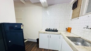 Eine kompakte Küche mit weißen Schränken, einem schwarzen Kühlschrank, einem Gasherd und einem Spülbecken.