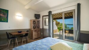 Een slaapkamer met een bed, een bureau, een stoel, een televisie en een schuifdeur die uitkomt op een buitenruimte met uitzicht op zee.