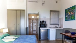 Een slaapkamer met een bed, een bureau, een magnetron en een kleine kitchenette.