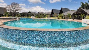 A swimming pool with a mosaic tile edge, surrounded by buildings with dark roofs and a clear blue sky. - Q Mango Forest Camping (Ramanagara)