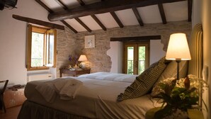 A bedroom with a stone wall, wooden beams, a bed with a white duvet, a bedside table with a lamp, and a window with a view of greenery. - Beautiful private villa for 6 people with WIFI, private pool, TV, patio and panoramic view (Tredozio)