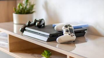 Een spelconsole en controllers op een houten tafel, met een kleine plant.