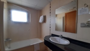 A bathroom with a bathtub, a sink, a mirror, and a window. - HOTEL AVENIDA (El Morell)