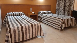 A hotel room with two beds, a nightstand with a phone, and a wall-mounted light fixture. - HOTEL AVENIDA (El Morell)