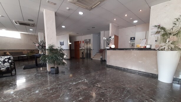A spacious lobby with a marble floor, a reception desk, and a seating area with a sofa and a chair. - HOTEL AVENIDA (El Morell)