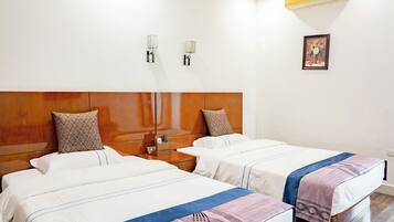 Een hotelkamer met twee bedden, houten hoofdborden, een nachtkastje en een airconditioner aan de muur, met een ingelijste foto.
