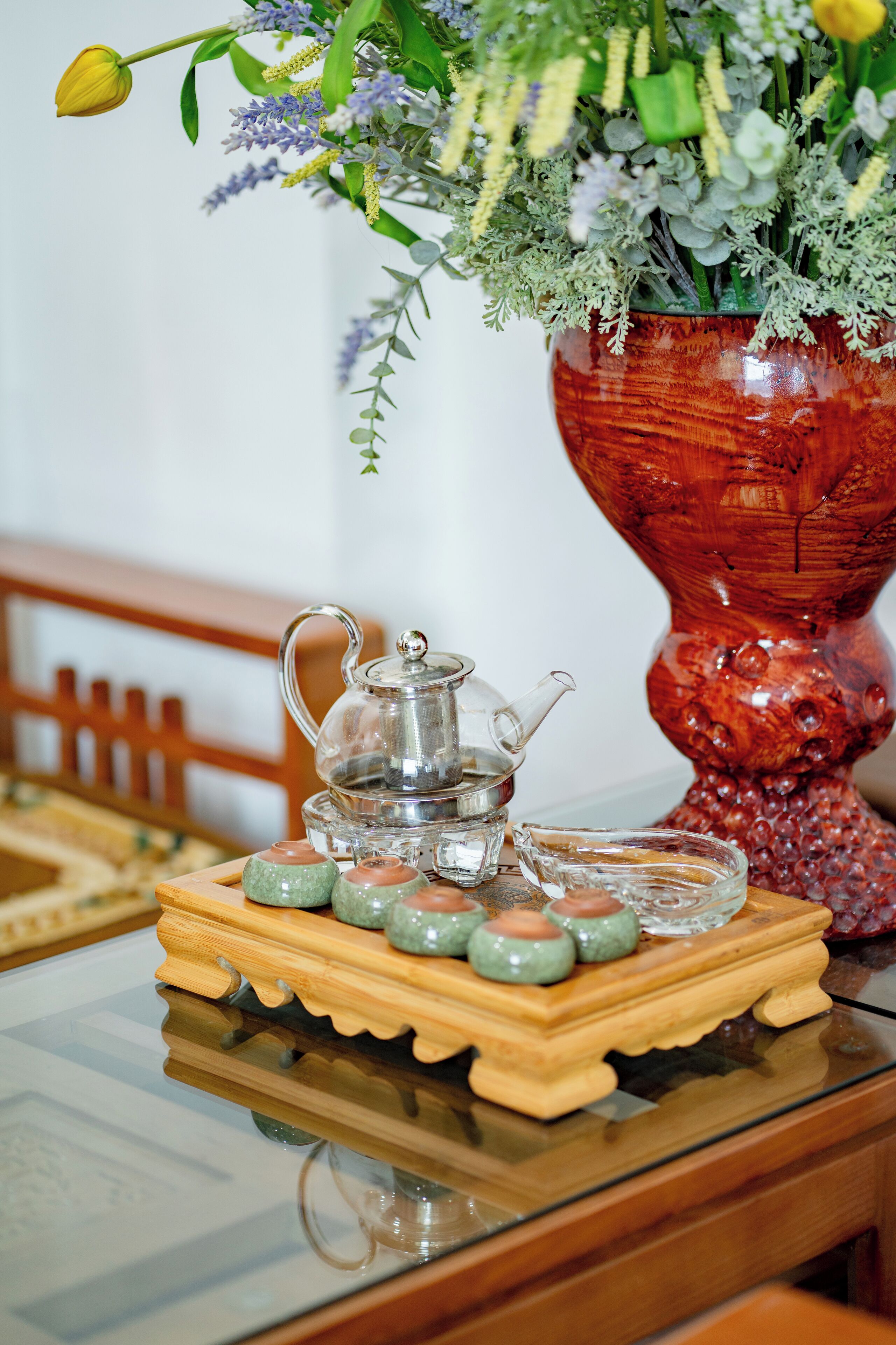 Una mesa con un juego de té, tazas y un arreglo floral en un florero decorativo.