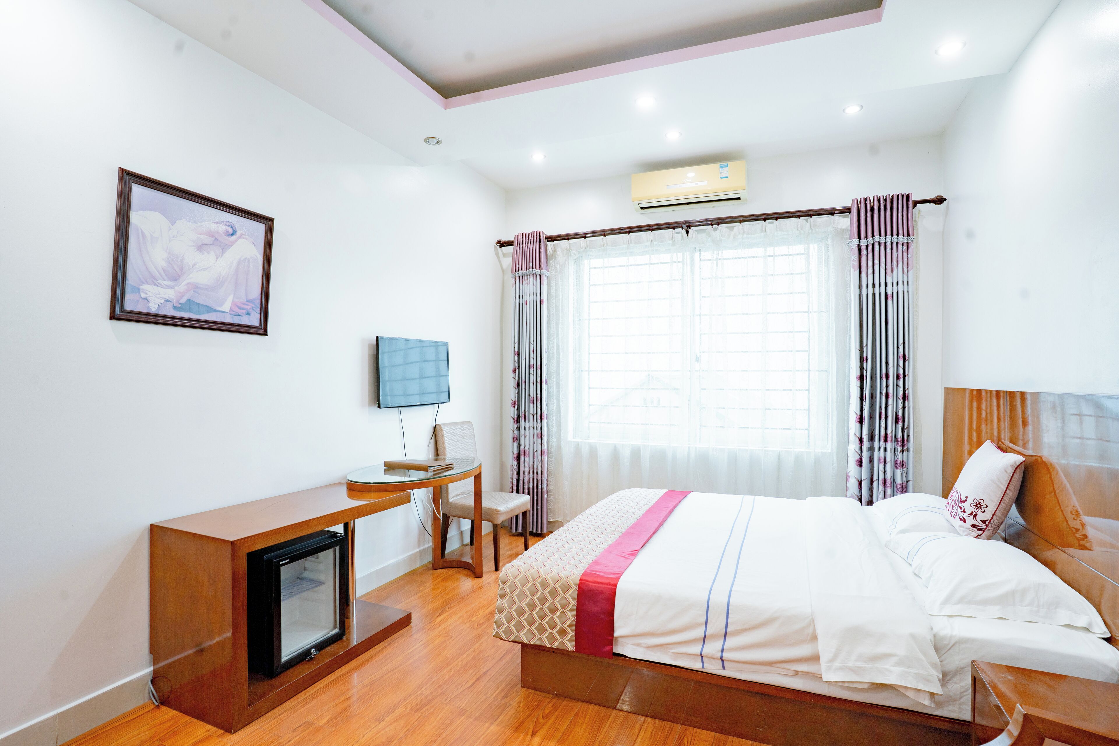Habitación de hotel con cama, escritorio, silla, televisión y aire acondicionado.