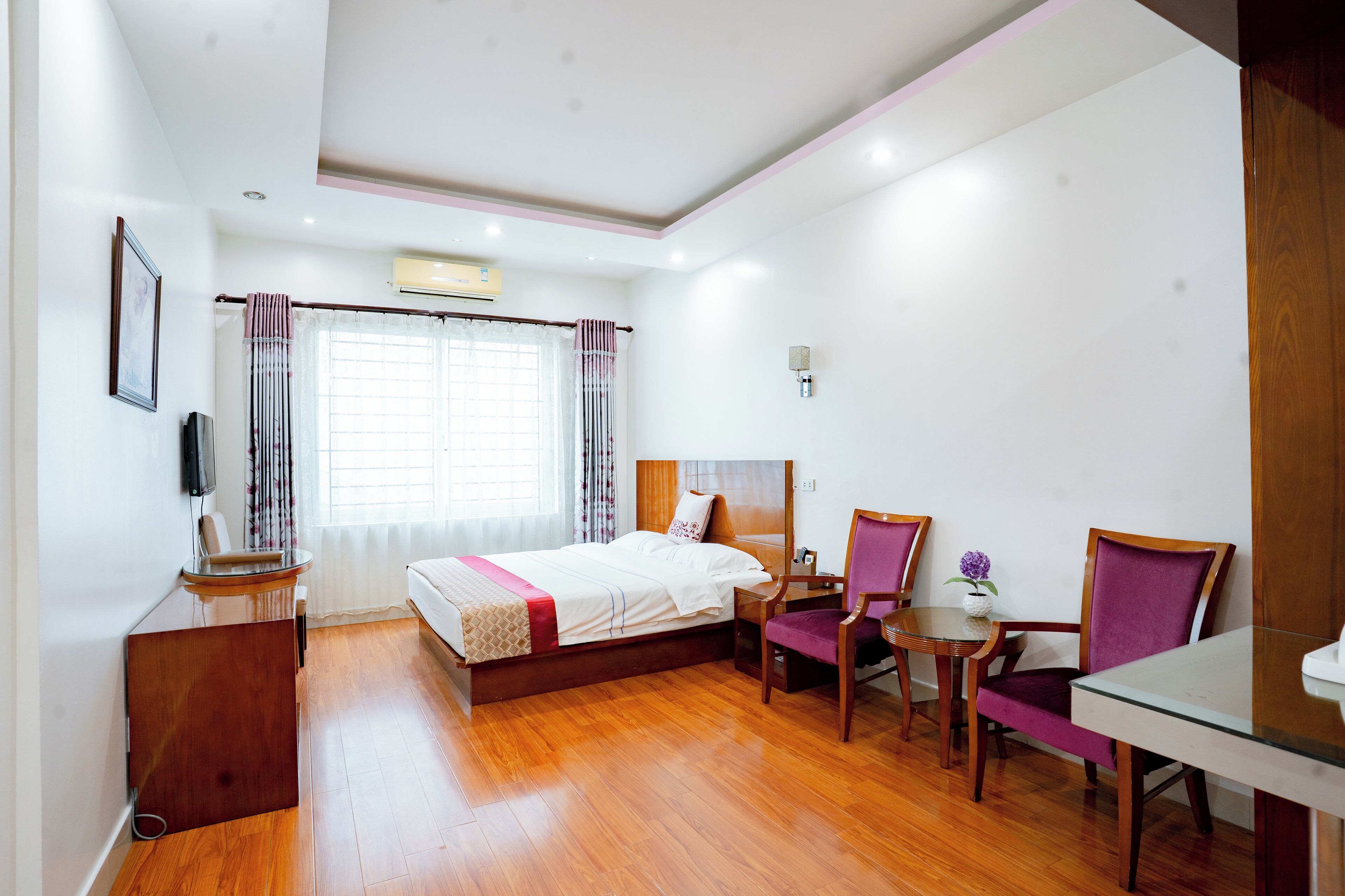 Habitación de hotel con suelo de madera, cama, escritorio, silla y una pequeña mesa.