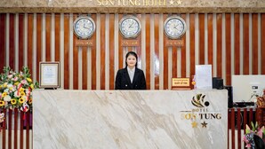 A hotel reception desk with clocks indicating different time zones, a framed certificate, and a floral arrangement. - Son Tung Hotel - Kim Dong Walking Street (Thuc Phan)