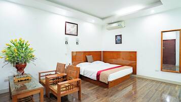 A hotel room with a wooden bed, a desk with a chair, a potted plant, and a mirror on the wall.